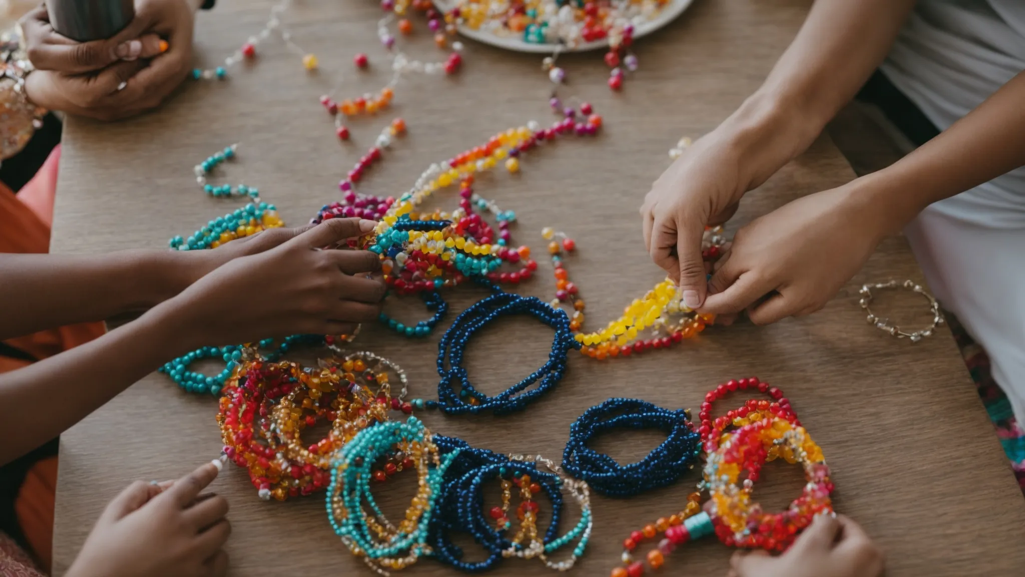 two people sitting at a table, working together to make colorful beaded bracelets from a diy kit.